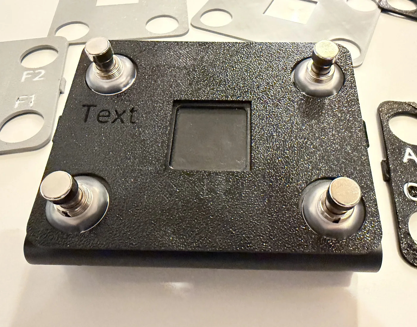 A Nano 4 with a black faceplate fitted, showing the screen cutout and switch cutouts, with unfitted plates beside it.